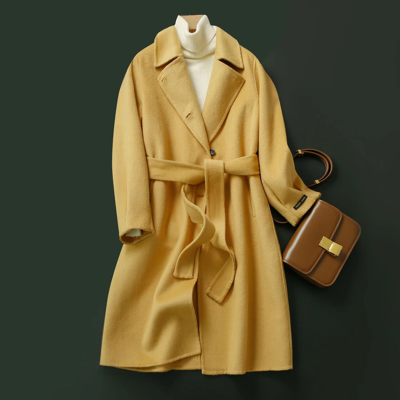 Belted Wool Wrap Coat — A long double-faced wool coat laid flat on a dark green ground, belted at the waist, in yellow and in cream
