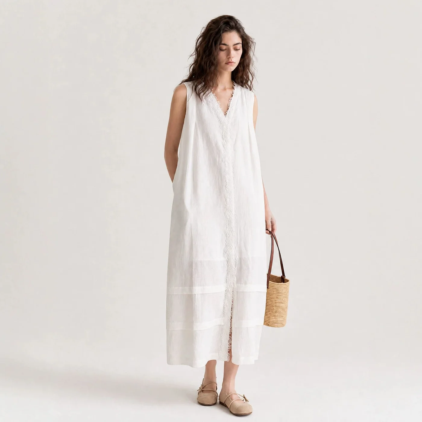Lace-Inset Linen Dress — A sleeveless ivory linen dress with a lace-edged V-neck worn by a model against a pale studio wall