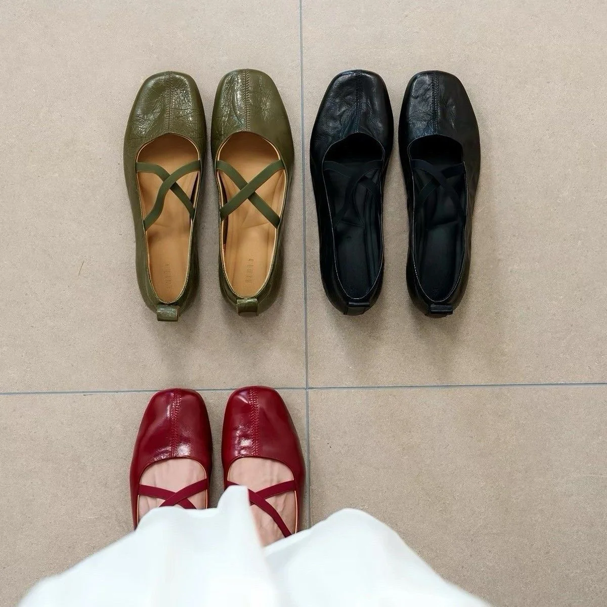 Square-Toe Criss-Cross Ballet Flat — A squared-toe leather ballet flat with two elastic bands crossing over the instep, shown in black, wine red and olive.